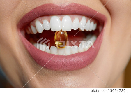 Cropped shot of woman with fish oil capsule in mouth. irl Holding Capsule With Omega-3 Between Teeth. Healthy Diet Nutrition. 136947894