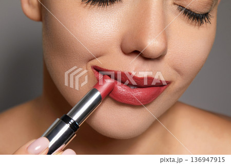 Woman applies lip balm in close-up shot showcasing her makeup and skincare routine at a spa 136947915