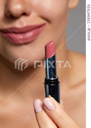 Woman applies nude lipstick while smiling in a skincare routine at a cosmetic studio with bright lighting Woman applies nude lipstick while smiling in a skincare routine at a cosmetic studio with bright lighting 136947916