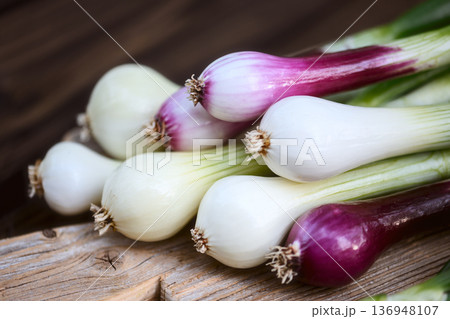Spring onions placed on wooden board over dark table Spring onions placed on wooden board over dark table 136948107