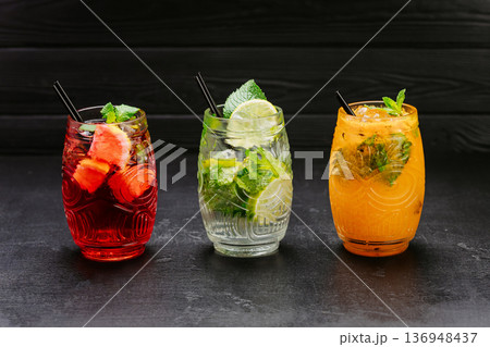 Colorful fresh cocktails with mint, lime and fruit served in glasses on dark background Colorful fresh cocktails with mint, lime and fruit served in glasses on dark background 136948437