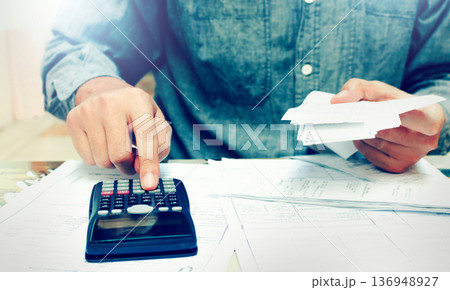 Young asian man using calculator and calculating bills to budgeting and tax calculation monthly expenses. budget management and accounting on table at home. 136948927