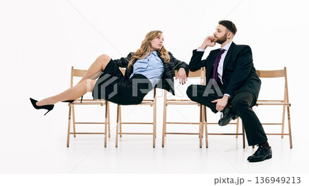 Elegant business couple posing across wooden chairs in white space. Elegant business couple posing across wooden chairs in white space. 136949213