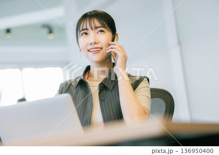 オフィスでノートパソコンを使いながら電話をする女性 136950400