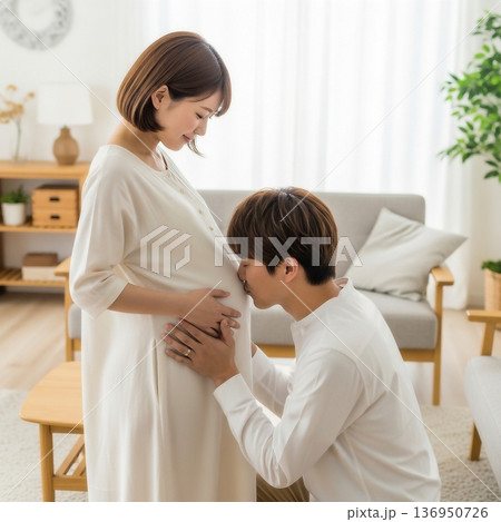 居間で妊娠した妻の大きなお腹に顔を寄せる夫 136950726