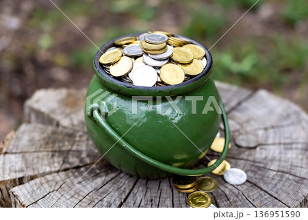 Green Pot Full of Golden and Silver Coins on a Rustic Wooden Stump 136951590