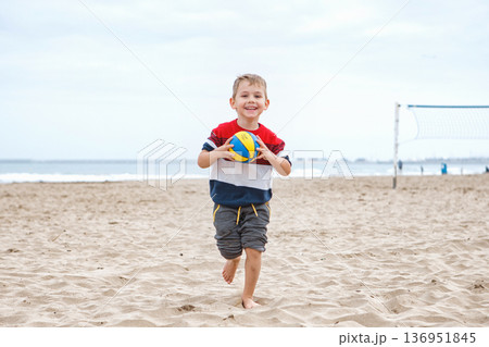 Happy Boy Running on the Beach With a Volleyball During a Cloudy Day Happy Boy Running on the Beach With a Volleyball During a Cloudy Day 136951845