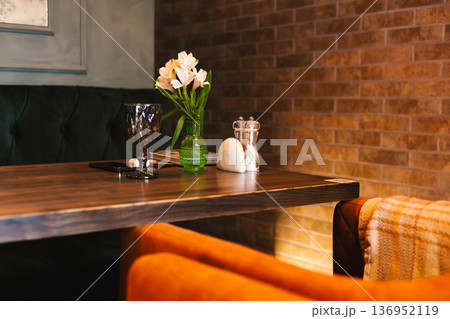 Cozy restaurant table setting with flowers in a green vase, a dark wine glass, and salt shakers. Moody atmospheric lighting with brick wall background Cozy restaurant table setting with flowers in a green vase, a dark wine glass, and salt shakers. Moody atmospheric lighting with brick wall background 136952119