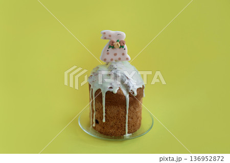 Bright Easter cake topped with white icing and bunny decoration on yellow background, cheerful spring celebration concept 136952872