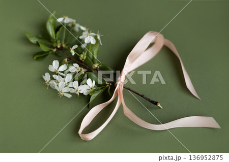 Blooming cherry blossom branch decorated with peach satin ribbon bow on pale green background, romantic spring composition Blooming cherry blossom branch decorated with peach satin ribbon bow on pale green background, romantic spring composition 136952875