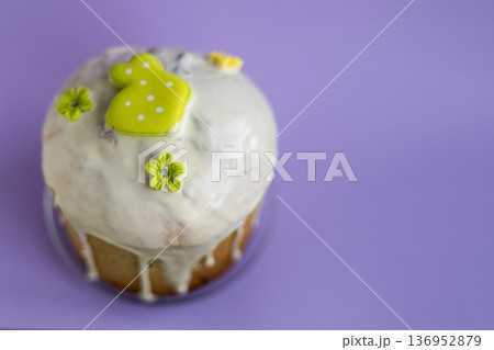Traditional Easter kulich with white icing and light green bunny topper on soft lavender background, festive spring dessert concept 136952879
