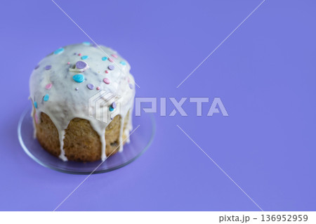 Traditional Easter cake covered with white icing and colorful sprinkles on purple backdrop, seasonal celebration styling 136952959