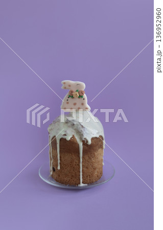 Easter cake with glossy icing and cute bunny ornament on soft lavender background, delicate pastel holiday mood 136952960
