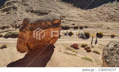 Aerial View of Two Hikers Walking Along Desert Trail Near Large Rock Formation Aerial View of Two Hikers Walking Along Desert Trail Near Large Rock Formation 136954237