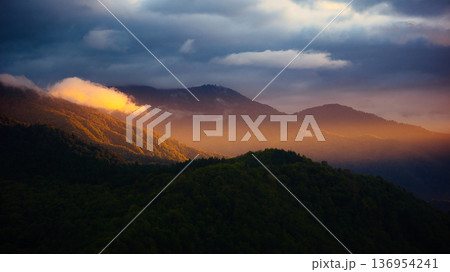 Golden Sunlight Breaking Through Clouds Over Mountain Forest at Sunset Golden Sunlight Breaking Through Clouds Over Mountain Forest at Sunset 136954241