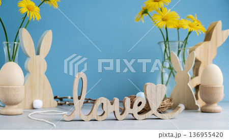 Wooden word LOVE with bunny figures eggs and fresh flowers. Easter composition content still life. Christian symbols of spring 136955420