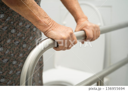 Asian elderly woman use toilet security support rail in bathroom. 136955694