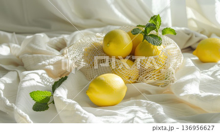 lemons in a mesh bag with mint leaves, lying on a white linen cloth, viewed from above on a sunny day with soft light, in a pastel aesthetic. lemons in a mesh bag with mint leaves, lying on a white linen cloth, viewed from above on a sunny day with soft light, in a pastel aesthetic. 136956627