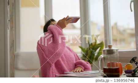 Young woman content creator taking coffee selfie in pink sweater 136956746