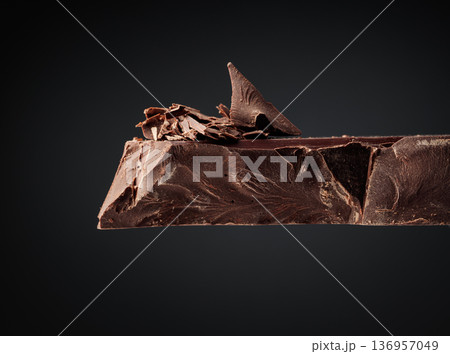 Large piece of dark chocolate and falling chocolate crumbs. 136957049