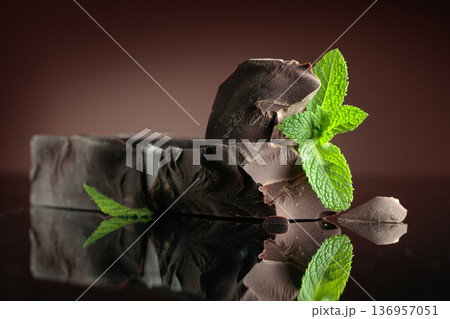 Large piece of dark bitter chocolate with mint on a black reflective background. Large piece of dark bitter chocolate with mint on a black reflective background. 136957051