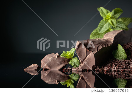 Pieces of dark bitter chocolate and chocolate chips with mint on a black reflective background. Pieces of dark bitter chocolate and chocolate chips with mint on a black reflective background. 136957053