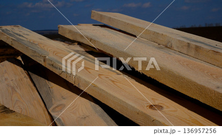 Wooden planks lie on the construction site against the background of a blue sky.  136957256