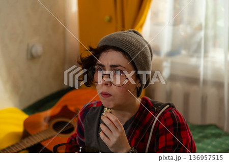 Portrait of Caucasian teenage woman student relaxing indoors with television. She sits on bed comfortably and eats popcorn. Home leisure idea. Portrait of Caucasian teenage woman student relaxing indoors with television. She sits on bed comfortably and eats popcorn. Home leisure idea. 136957515