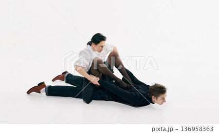 Stylish woman holding man arms while sitting on him in white studio composition. 136958363