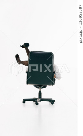 Female figure partially concealed by office chair with raised legs in minimal studio. 136958397