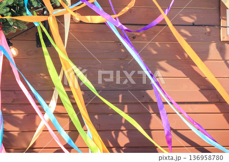 Spring festival bright satin ribbons hanging against a brown wooden wall background with copy space. Spring festival bright satin ribbons hanging against a brown wooden wall background with copy space. 136958780