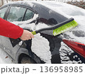 Person brushing fresh snow off black car with green snow brush on cold winter day. 136958985