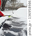 Person brushing fresh snow off black car with green snow brush on cold winter day. 136958986