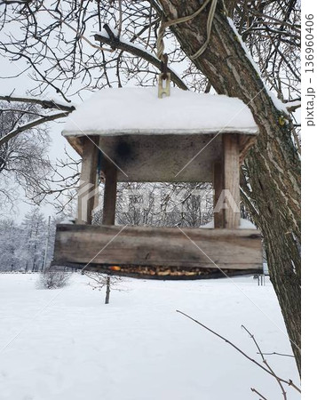 Rustic wooden bird feeder hanging on tree branch covered with fresh snow in winter landscape. 136960406