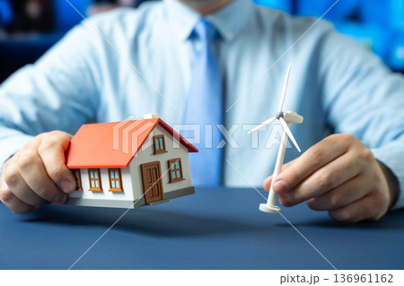 House and windmill in the hands of a man. Autonomous housing powered by renewable energy. Sustainable living and home independence. Green technology for households and energy efficiency 136961162