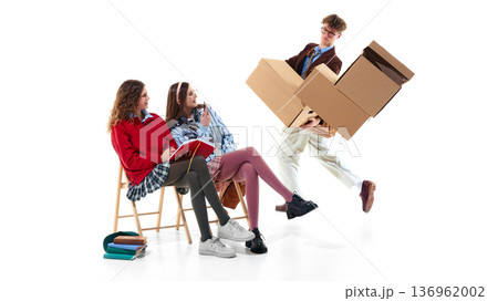 Teen students in preppy outfits reacting to boy with falling boxes isolated on white Teen students in preppy outfits reacting to boy with falling boxes isolated on white 136962002