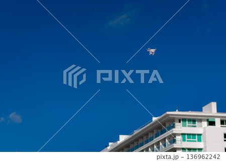 White drone flying above modern building against deep blue sky White drone flying above modern building against deep blue sky 136962242