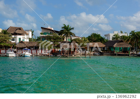 Tropical waterfront with thatched roof huts and docked boats 136962292