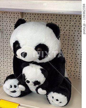 Plush panda toy holding smaller panda on shelf. Childhood comfort, gift idea, innocence concept, retail display, softness and tenderness 136962394