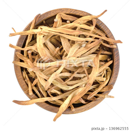 Top view of dried lily buds, also known as golden needles or huang hua cai, in a dark wooden bowl isolated. Traditional Chinese culinary ingredient for soups and stir-fry. Top view of dried lily buds, also known as golden needles or huang hua cai, in a dark wooden bowl isolated. Traditional Chinese culinary ingredient for soups and stir-fry. 136962555