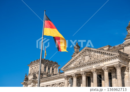 Berlin, germany, august 15, 2023. The german national flag waving in front of the historic reichstag building under a clear blue sky, symbolizing government and democracy 136962713