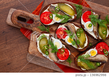 open sandwiches with sprats, vegetables and herbs, on a wooden board, breakfast, snack, 136962998
