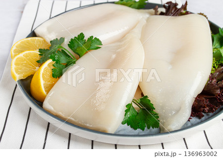 Fresh squid on a black plate with greens and lemon slices prepared for cooking in a kitchen setting 136963002