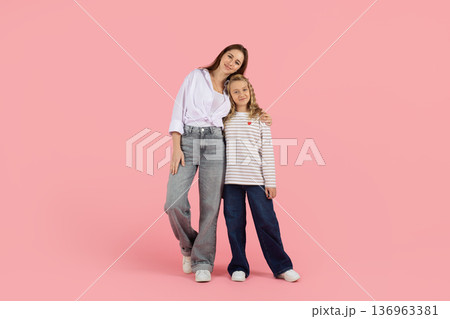 Smiling caucasian mother and daughter standing together on pink studio background Smiling caucasian mother and daughter standing together on pink studio background 136963381