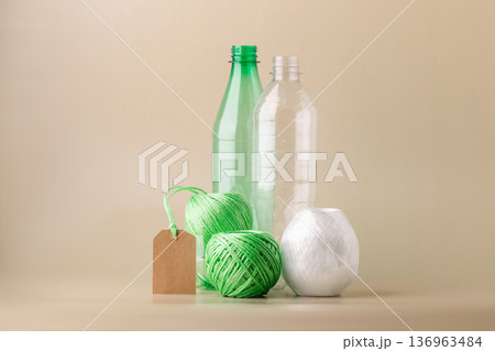 Empty plastic bottles, several skeins of polyester thread, blank label promoting recycling, sustainability, eco-friendly production. Green lifestyle, eco-technologies Empty plastic bottles, several skeins of polyester thread, blank label promoting recycling, sustainability, eco-friendly production. Green lifestyle, eco-technologies 136963484