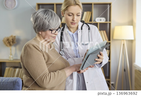 Doctor advising senior woman on tablet during home visit and healthcare support Doctor advising senior woman on tablet during home visit and healthcare support 136963692