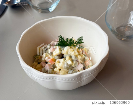 Close-up traditional russian salad in white bowl with dill garnish. Comfort food, festive cuisine and homemade dining tradition. Close-up traditional russian salad in white bowl with dill garnish. Comfort food, festive cuisine and homemade dining tradition. 136963960
