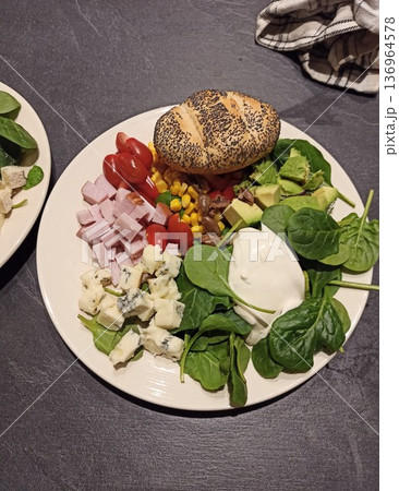 Fresh salad bowl with spinach avocado tomato corn ham cheese and poppy seed bun on plate. Healthy lunch concept of balanced diet nutrition and homemade meal Fresh salad bowl with spinach avocado tomato corn ham cheese and poppy seed bun on plate. Healthy lunch concept of balanced diet nutrition and homemade meal 136964578