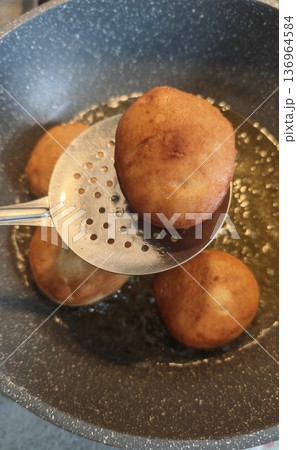 Fried donut cooking in hot oil with skimmer in pan. Close up bakery concept of homemade dessert street food and deep frying process 136964584