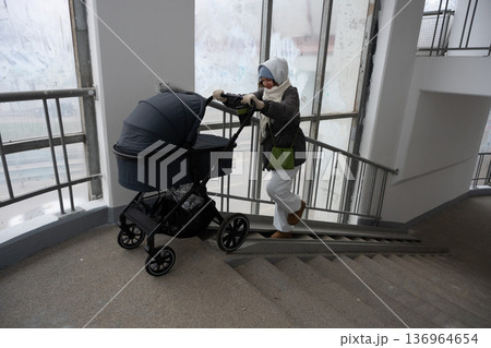 Young mother pushing stroller up residential building stairs 136964654